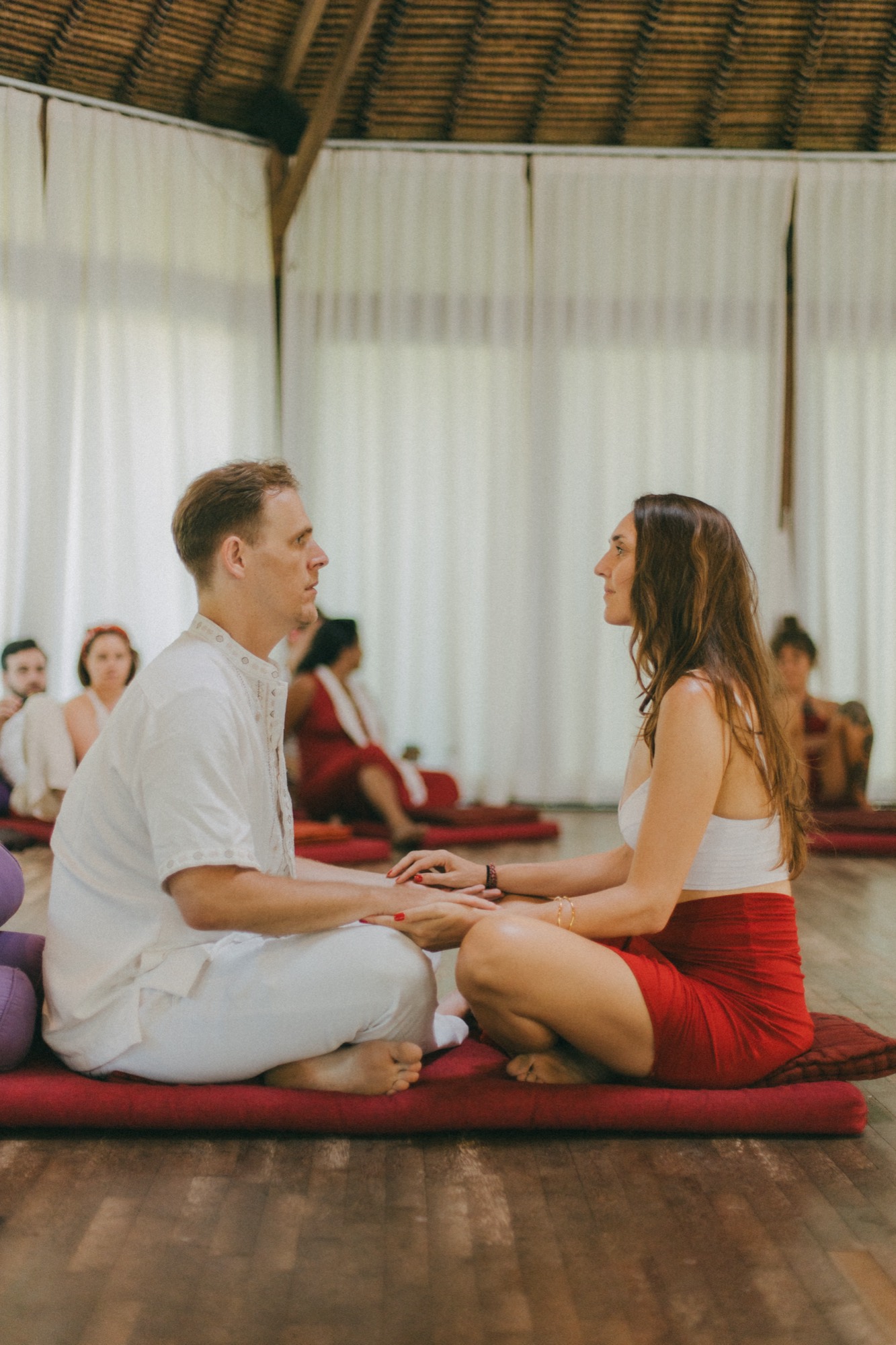 Two retreat participants sitting face to face, hands joined, in a moment of paired Tantric practice